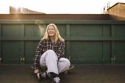 Portrait of smiling teenage girl sitting on skateboard