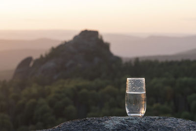 Close-up of drink on rock against sky at sunset