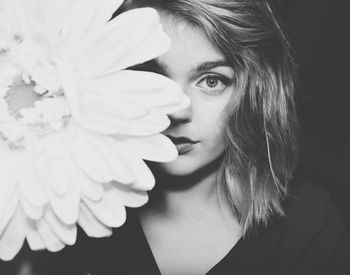 Close-up portrait of beautiful woman behind flower against black background