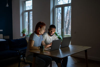 Young interracial couple looking at laptop discussing online family business, working late at home