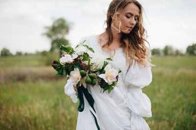 Bride holding bouquet while standing on field