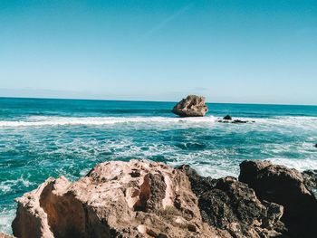 Scenic view of rocks in sea against clear blue sky