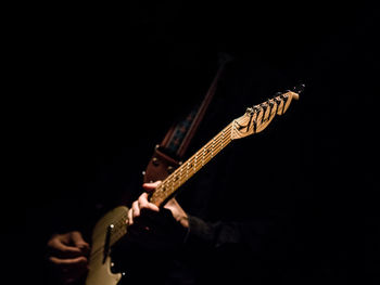 Close-up of person playing guitar against black background