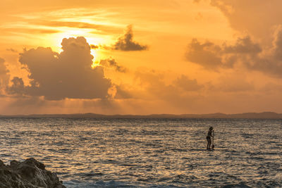 Silhouette man standing in sea against sky during sunset