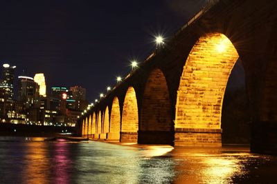 Illuminated bridge over water in city against sky at night