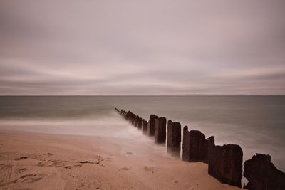 Groyne at sea against sky during sunset