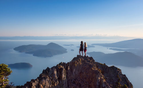 People standing on rock against sky during sunset