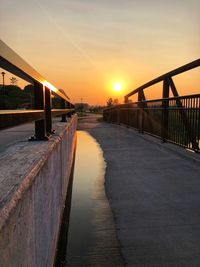 Footbridge over canal against sky during sunset