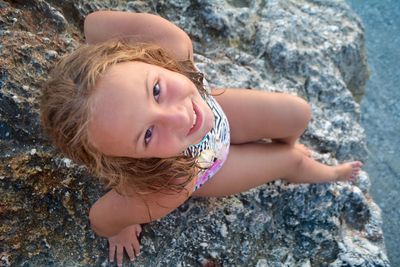 High angle portrait of smiling girl sitting on rock