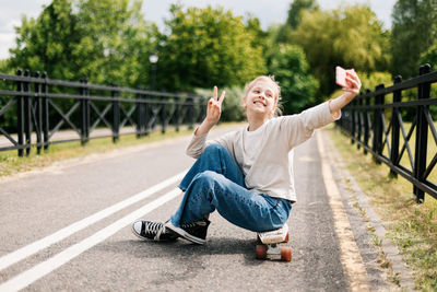 Cute blonde teenage girl sitting on a skateboard in a city park 