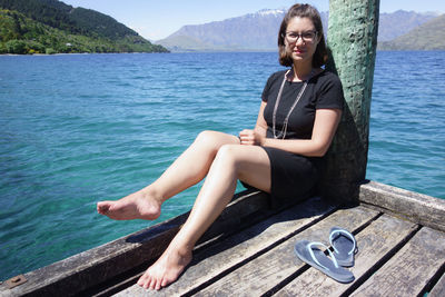 Portrait of young woman sitting on pier over sea