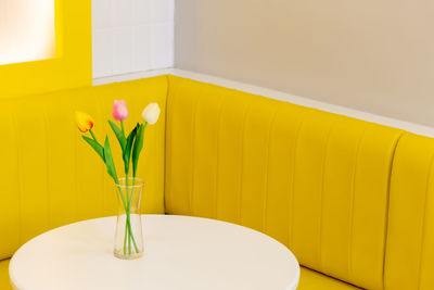 Close-up of yellow rose in vase on table against wall at home