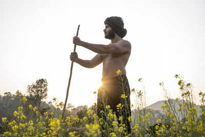 Full length of man standing on yellow flowering plant against clear sky