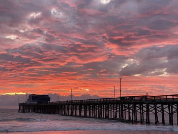 Pier over sea against dramatic sky during sunset