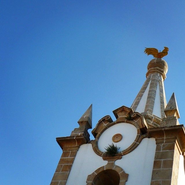 low angle view, clear sky, architecture, built structure, copy space, building exterior, sculpture, statue, blue, art and craft, human representation, art, creativity, history, high section, day, religion, animal representation, no people