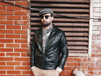 Mid adult man wearing sunglasses standing against brick wall