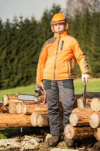 Full length of man holding chainsaw while standing against logs