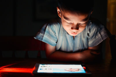 Boy sitting and looking at an ipad on table in the dark