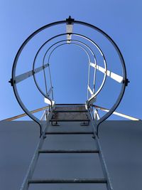 Low angle view of ladder by wall against clear blue sky