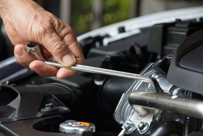 Cropped hand of mechanic repairing car engine with wrench