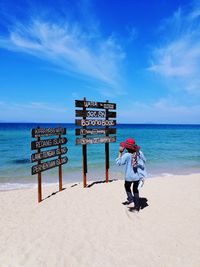 Full length of woman standing by information sign at beach