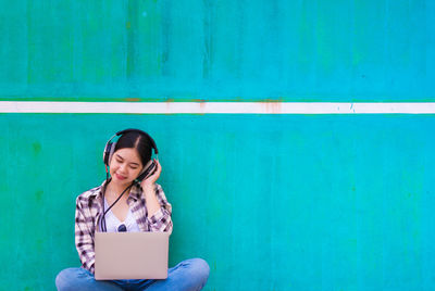 Young woman using laptop against blue wall