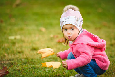 Full length of cute girl holding maple leaf during autumn sitting on grass at park
