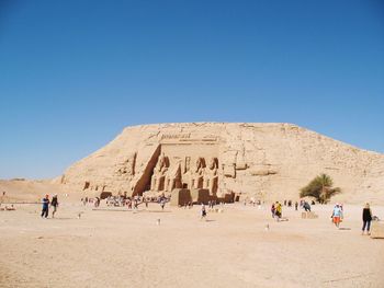 People visiting old ruin against clear blue sky during sunny day