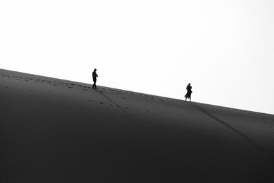 Silhouette man walking on beach against clear sky