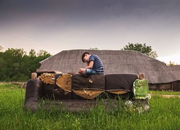 Man sitting on sofa in field against sky