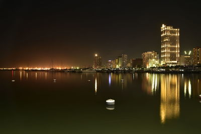 Illuminated cityscape by sea against sky at night