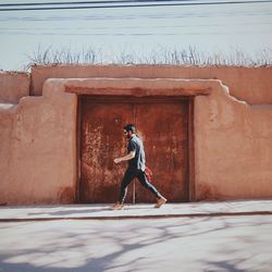 Full length of man walking by doorway on sidewalk during sunny day