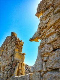 Low angle view of damaged stone wall against clear blue sky