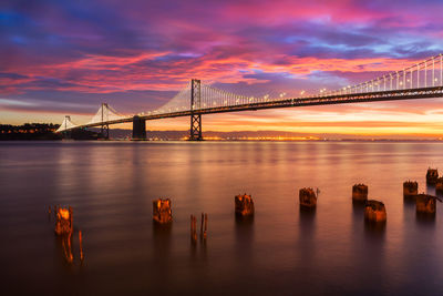 Wooden post on river with suspension bridge at dusk