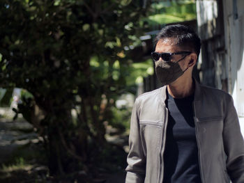 Portrait of young man wearing sunglasses standing against trees