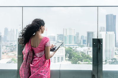 Rear view of businesswoman using digital tablet while standing by railing