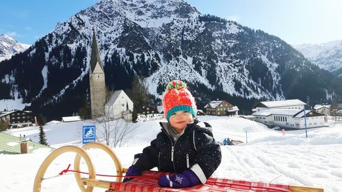 Portrait of baby girl with sled on snow covered landscape