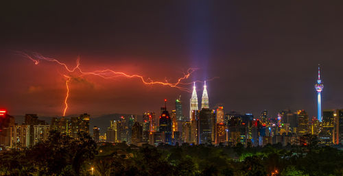 Illuminated cityscape against sky at night with lightning strikes across the skyline 