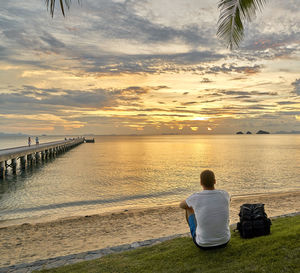 Rear view of man sitting at beach during sunset