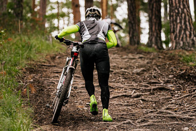 Rear view of man walking with bicycle in forest