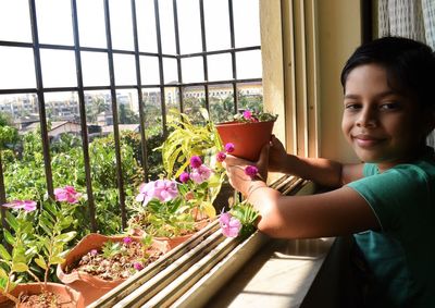 Portrait of woman holding potted plant by window