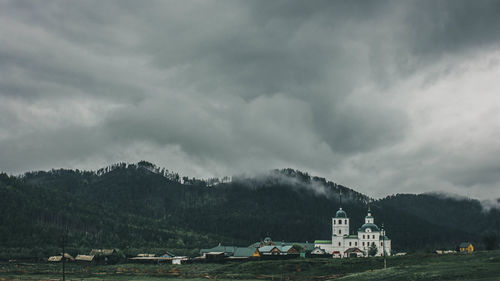 Houses on mountain against storm clouds