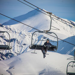 Low angle view of woman sitting on ski lift against snowcapped mountains