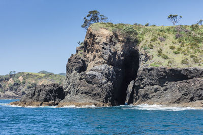 Scenic view of rocks by sea against clear blue sky