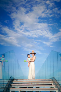 Woman standing on railing against sky