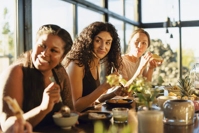 Smiling female friends looking away while sitting with breakfast at dining table