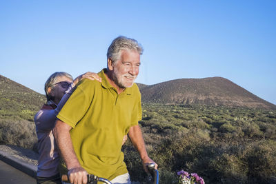 Senior couple riding bicycle on road against landscape