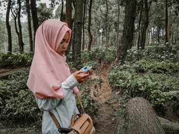 Woman wearing hijab while using mobile phone in forest