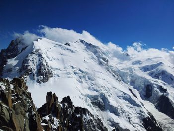 Low angle view of snowcapped mountains against blue sky