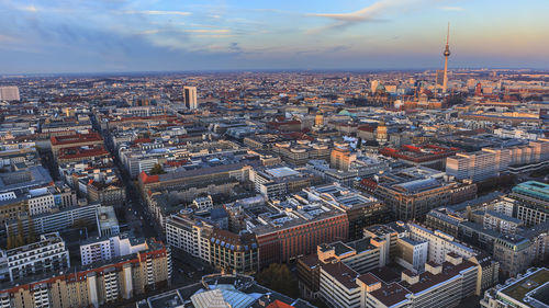 Fernsehturm amidst cityscape against sky during sunset